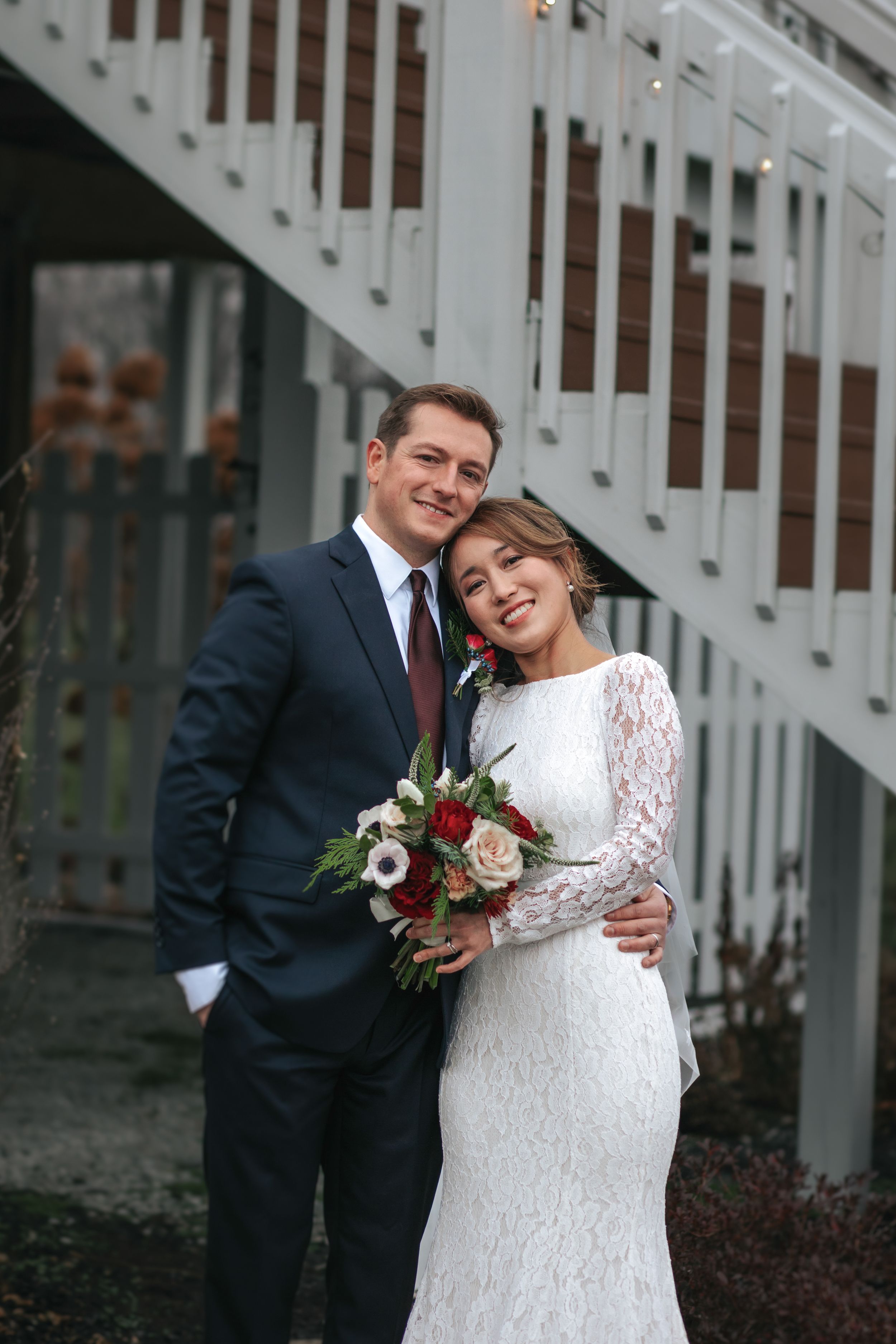 A couple in wedding attire share intimate moments in front of a white staircase.