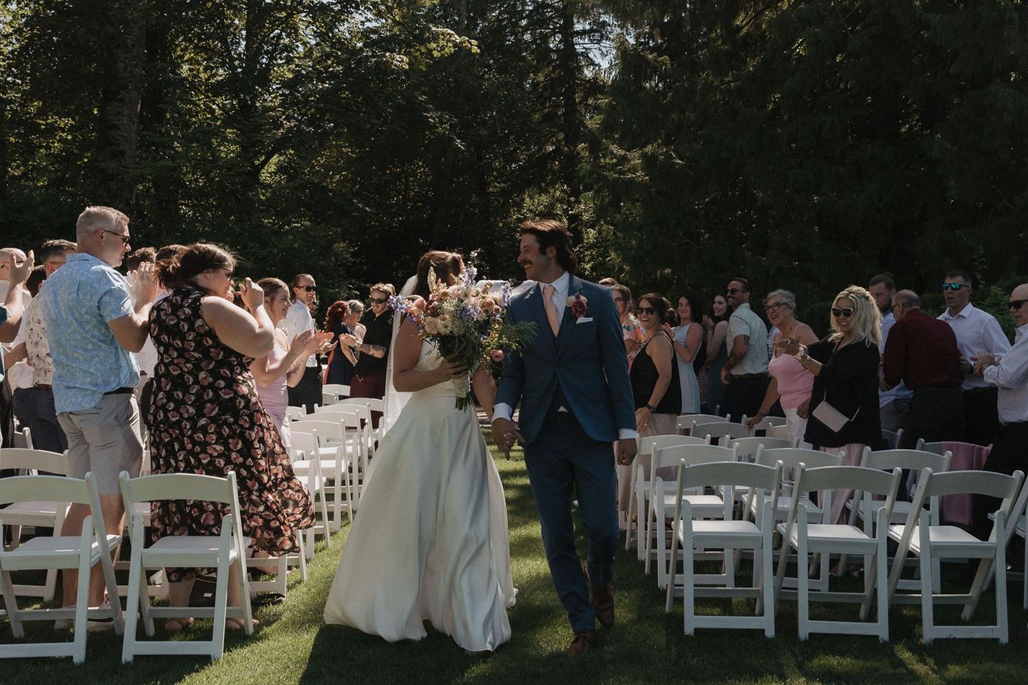 Bride and groom walk back down the aisle after outdoor wedding ceremony surrounded by cheering guests.
