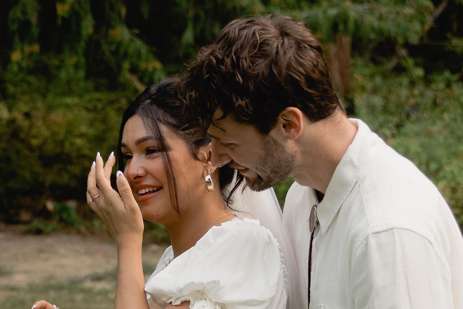 Joyful bride and groom laugh together closely in an intimate outdoor wedding portrait.