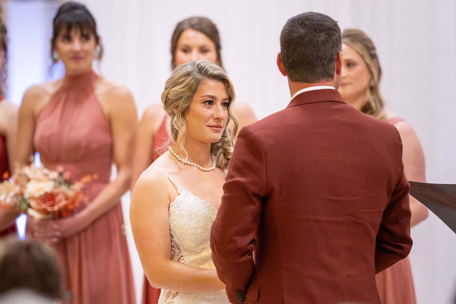Wedding ceremony scene with bridesmaids in dusty rose dresses and groomsmen in burgundy suits dancing at reception.