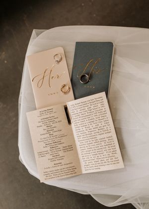 Wedding vows and rings displayed on elegant cream and navy blue cards with delicate veil fabric in the background.