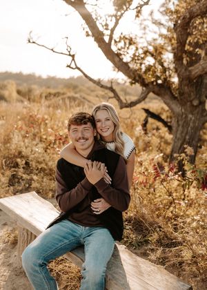 A couple shares joyful moments together on a rustic wooden bench surrounded by golden autumn foliage.