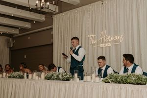 Wedding reception venue decorated with white drapes, exposed wooden beams, and elegant chandeliers for an indoor celebration.