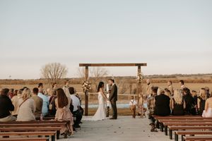 Outdoor wedding ceremony setup with wooden benches arranged in rows facing an altar in a rural setting.