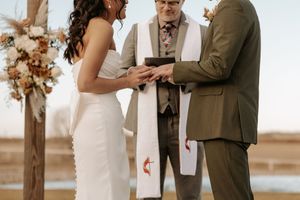 A couple exchanges vows during an outdoor wedding ceremony with water in the background and floral arrangements.