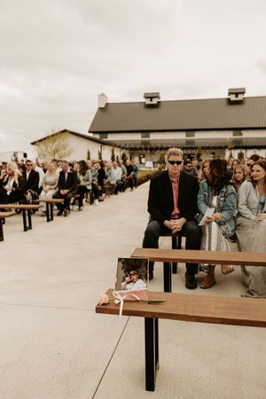 Outdoor wedding ceremony setup with guests seated on benches in front of a rustic barn.