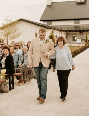 Wedding processional on outdoor concrete path with barn venue in background.