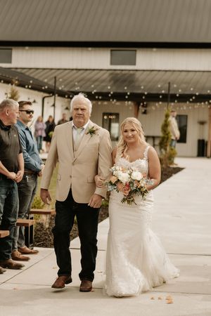 A touching wedding ceremony moment as a bride in a fitted lace gown walks down an outdoor aisle with an escort.