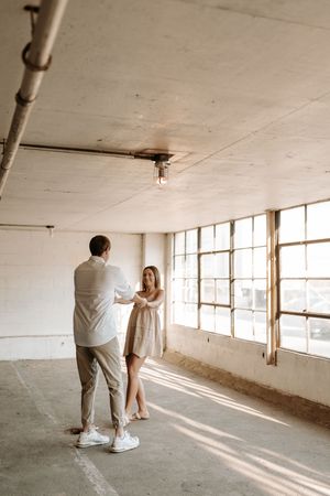 Couple walking through a sunlit empty industrial space with large windows casting dramatic shadows.