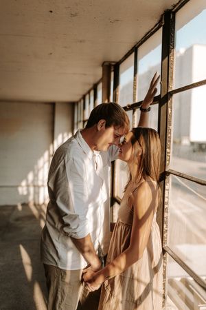A couple shares tender moments near sunlit windows in an industrial setting.