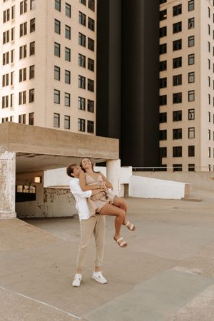 A couple performs playful dance moves in an urban setting with tall buildings in the background.