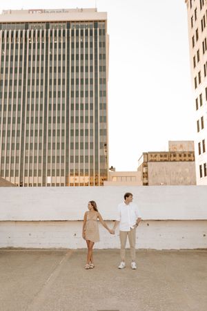 Romantic couple posing against urban backdrop with tall office buildings in soft natural light.