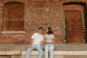 Couple sitting together on rustic brick ledge in casual denim outfits.