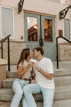 A couple in white and light blue outfits share affectionate moments on outdoor steps.