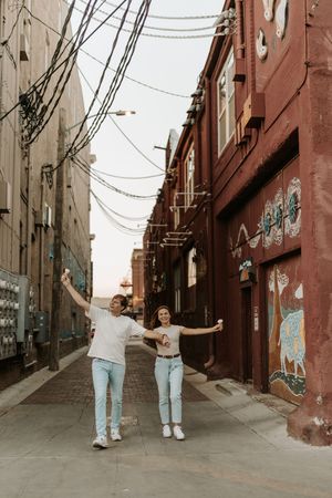 Four sequential photos showing two people walking and posing playfully in an urban alley with brick buildings.