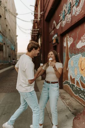 Playful couple dancing in urban alley with colorful graffiti wall backdrop.