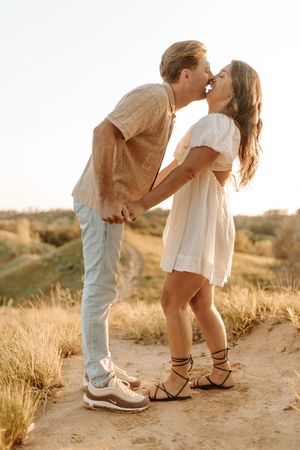 A couple sharing a romantic kiss in a desert landscape at golden hour, shown in a series of close-up shots of their feet.