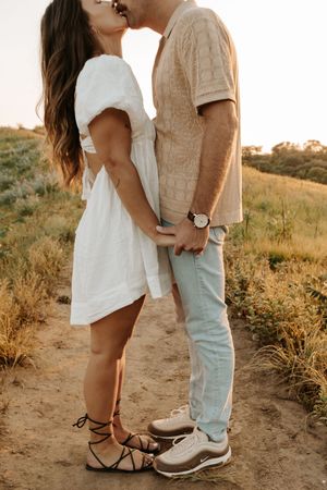 A romantic couple embracing on a dirt path during golden hour with dried grass and brush in the background.