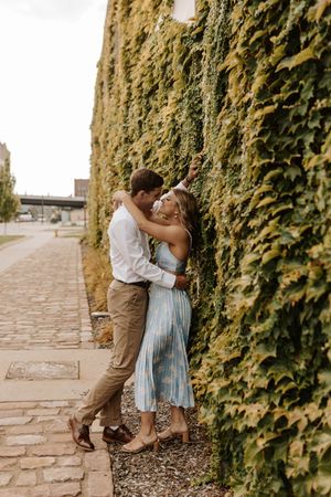 A couple in casual attire shares romantic moments against a backdrop of ivy-covered stone walls.