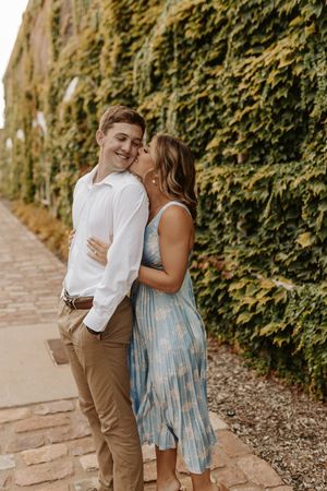 A romantic couple shares tender moments along an ivy-covered stone wall path in summer attire.