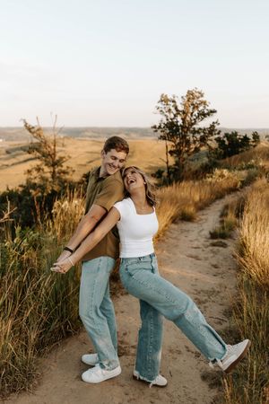 Couple playfully posing on a hilltop hiking trail at golden hour with rolling hills in the background.
