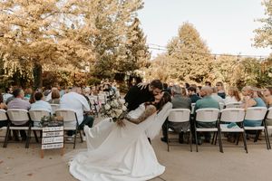A couple shares their first dance at an outdoor wedding reception surrounded by seated guests in a wooded setting.