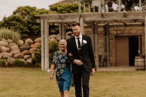 Wedding couple walks together along rustic barn venue path surrounded by natural stone landscaping.