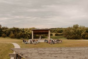 Rustic outdoor amphitheater with wooden benches and covered stage area surrounded by green countryside.