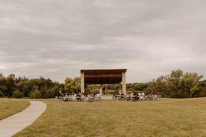 A panoramic view of a rural landscape with a winding path and shelter structure under cloudy skies.