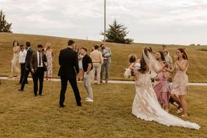Wedding party members gather on a grassy hill during golden hour for outdoor photos.