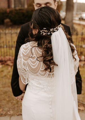 Close-up details of a bride's lace wedding dress with pearl embellishments and flowing veil against an autumn backdrop.