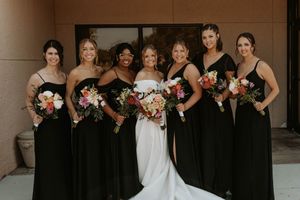 Wedding party in black bridesmaid dresses and white bridal gown pose together for formal portrait.