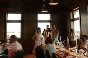 A group of people gather in a dimly lit restaurant space with large windows and pendant lighting.