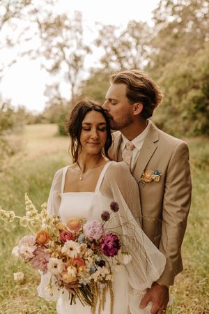 A romantic outdoor wedding photoshoot featuring a couple in a meadow with a beautiful floral bouquet.