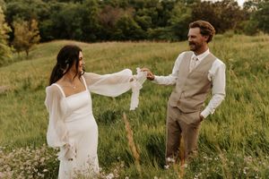A couple shares a playful moment in a sunlit meadow during their rustic outdoor wedding celebration.