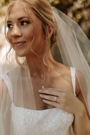 Close up details of a bride in white lace dress with flowing veil against warm background.