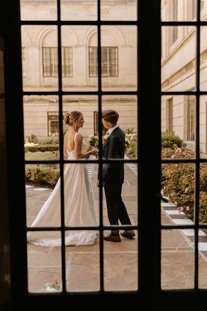 A wedding couple framed through window panes in an artistic black and white composition.