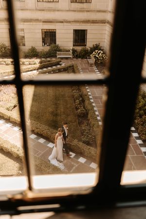 Aerial view through window panes showing a bride walking on a stone pathway in sepia tones.