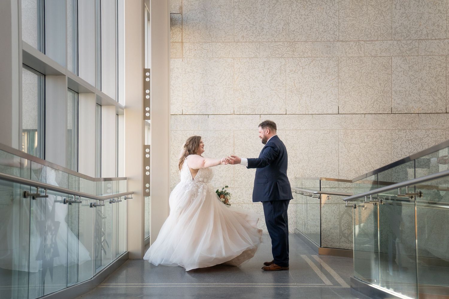 A bride and groom share an intimate moment in a modern hallway with glass walls and stone textures.