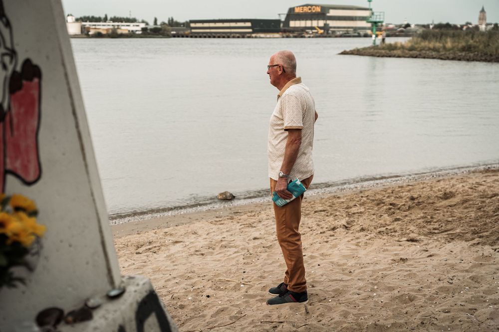 Someone stands on a sandy beach near an industrial waterfront area on an overcast day.