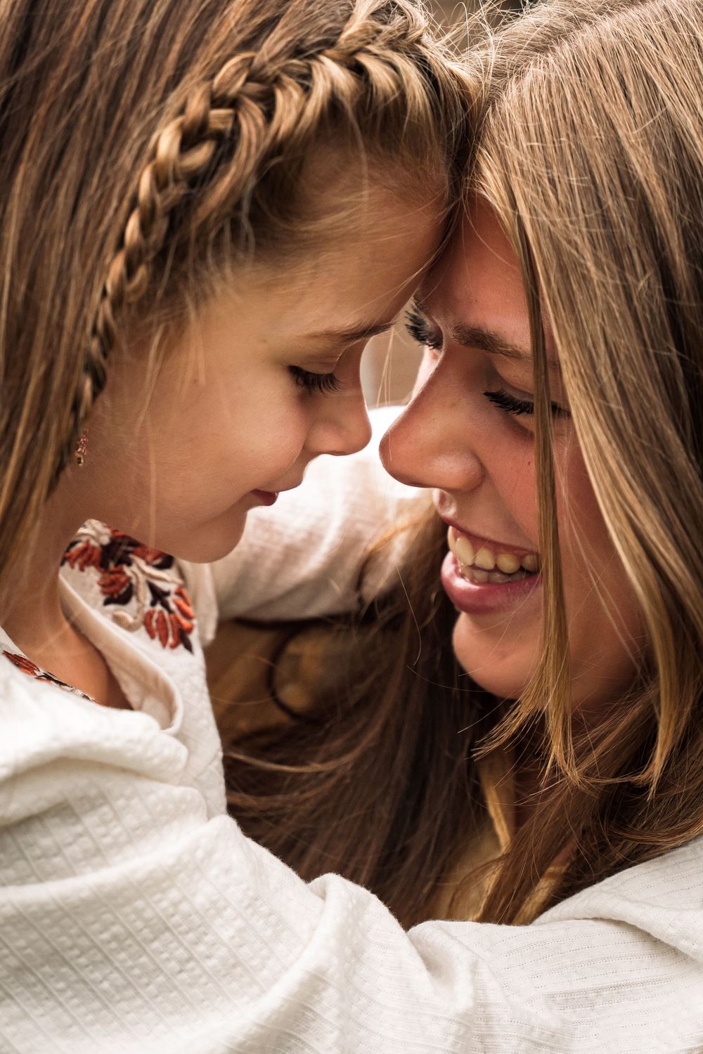 Two people share an intimate moment in white clothing, with one wearing a braided hairstyle and embroidered detail.