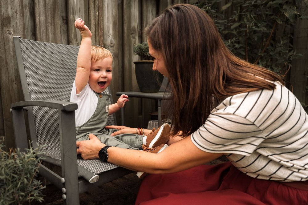 A candid outdoor moment of interaction between an adult in stripes and an excited toddler sitting on a wooden bench.