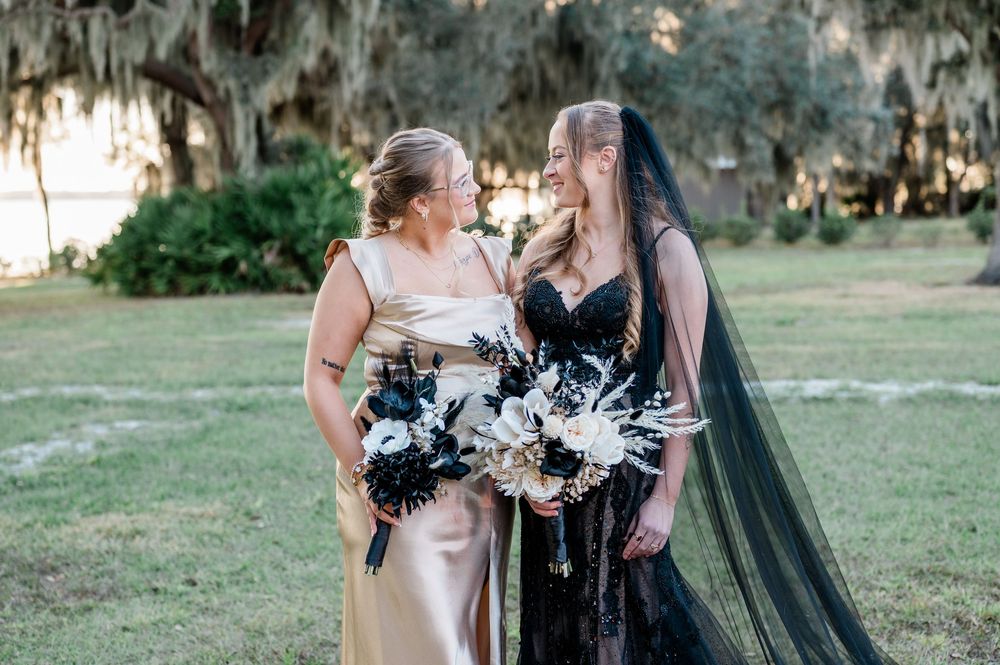 Two people in wedding attire embrace outdoors with Spanish moss hanging from trees in the background.