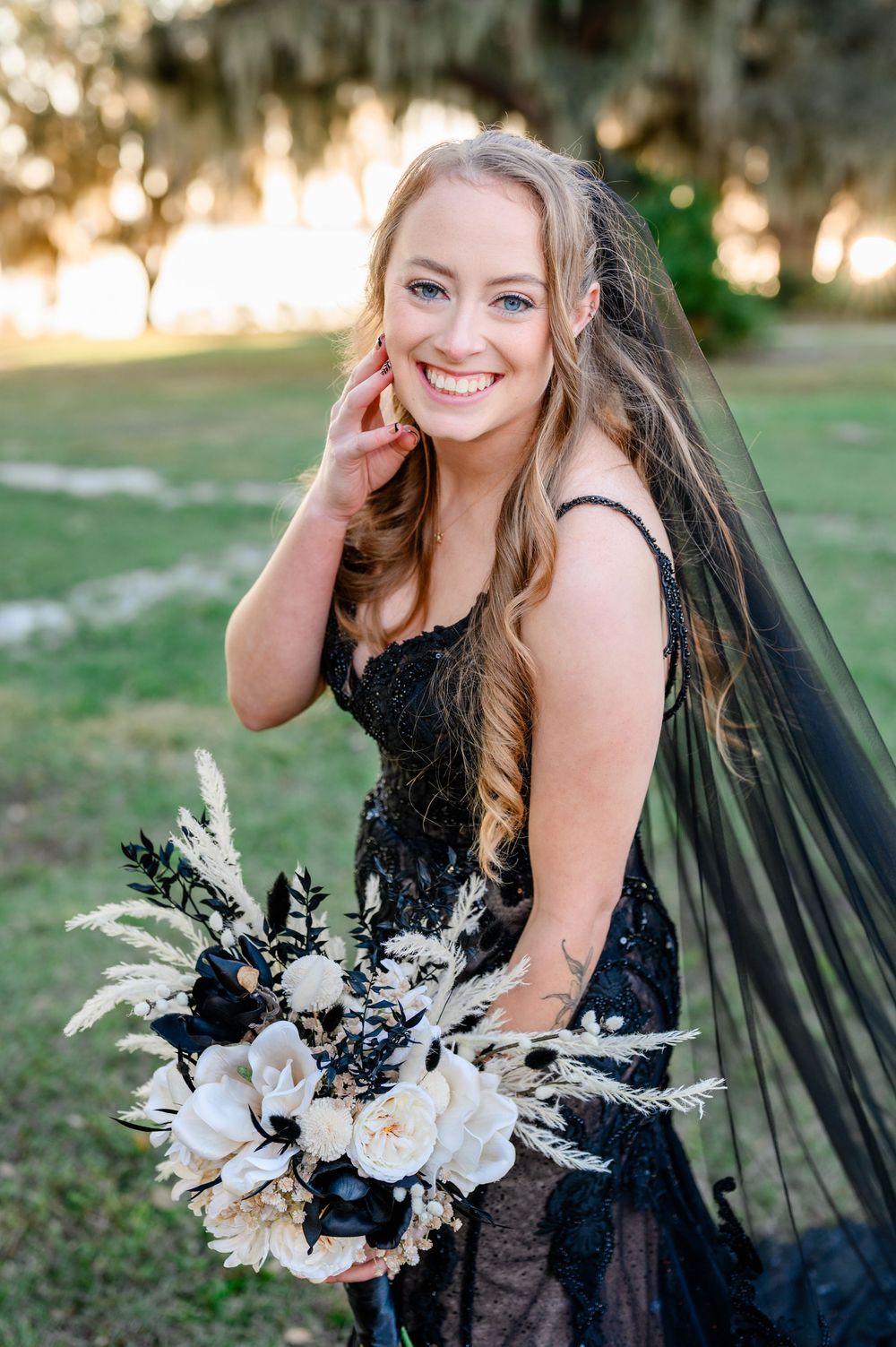 Romantic bridal portraits in a grassy field with a black lace gown and white bouquet at sunset.