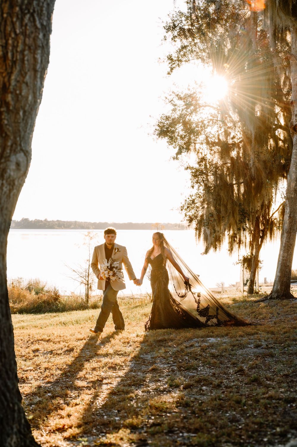 Couple dancing and playing in golden sunlight beneath Spanish moss draped trees at sunset by a lake.