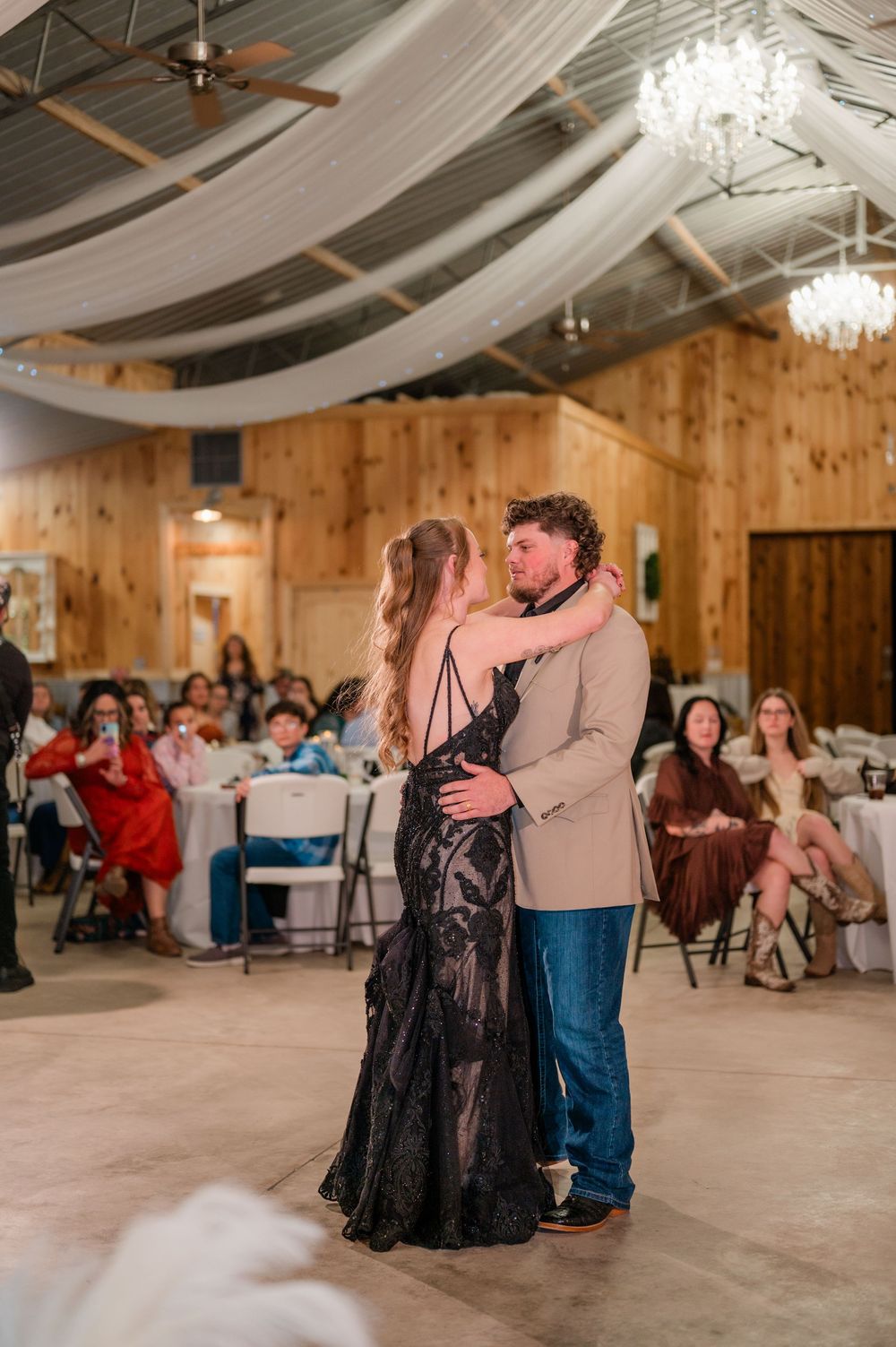 Couples dancing at a rustic wedding reception venue with wooden walls and draped fabric ceiling decor.
