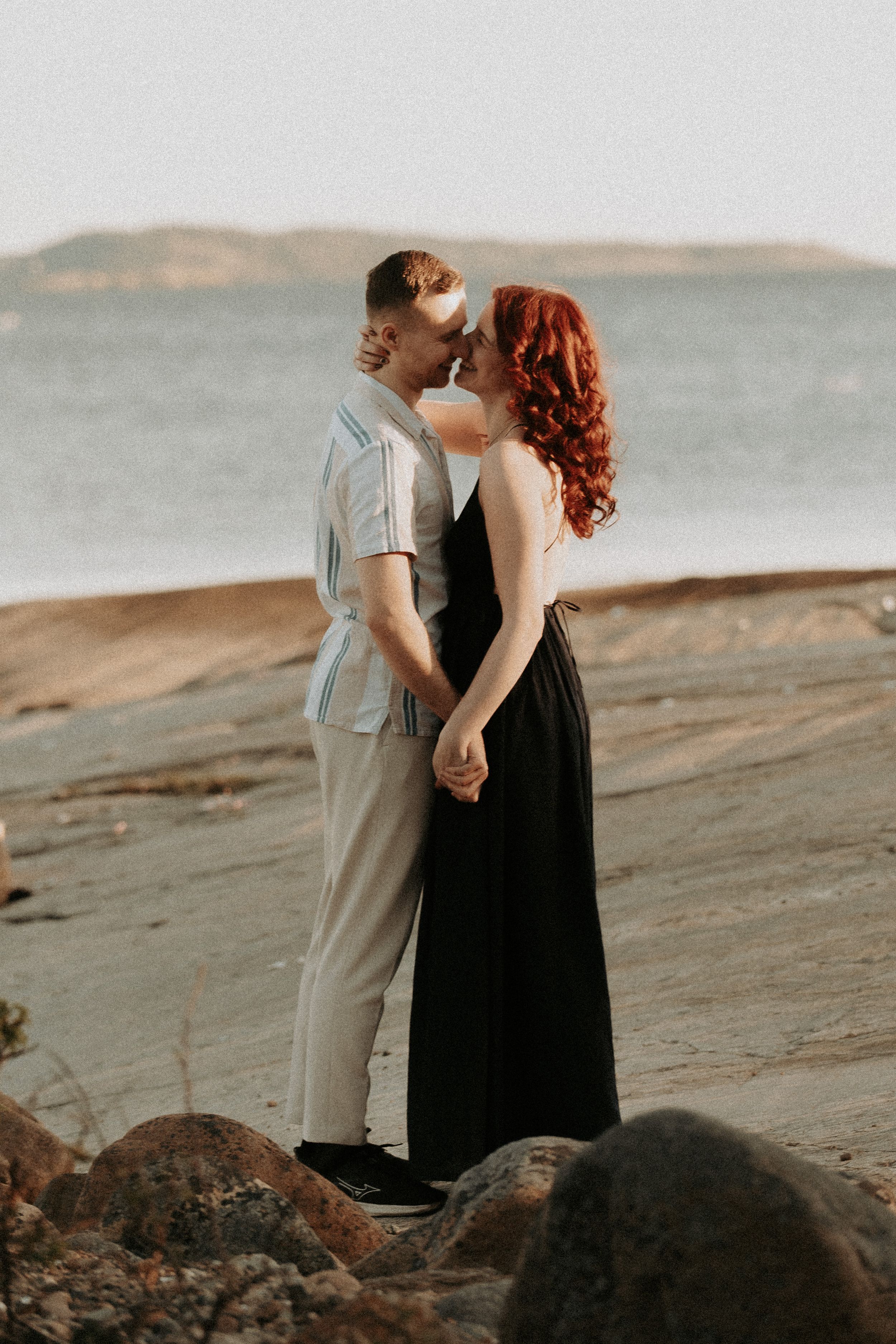 Couple shares an intimate moment on rocky coastal shoreline at sunset.