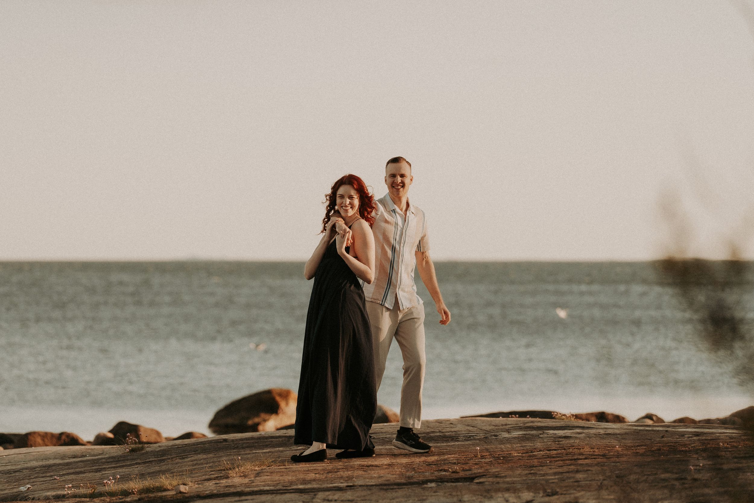 Two people walk together along a scenic rocky beach at dusk.