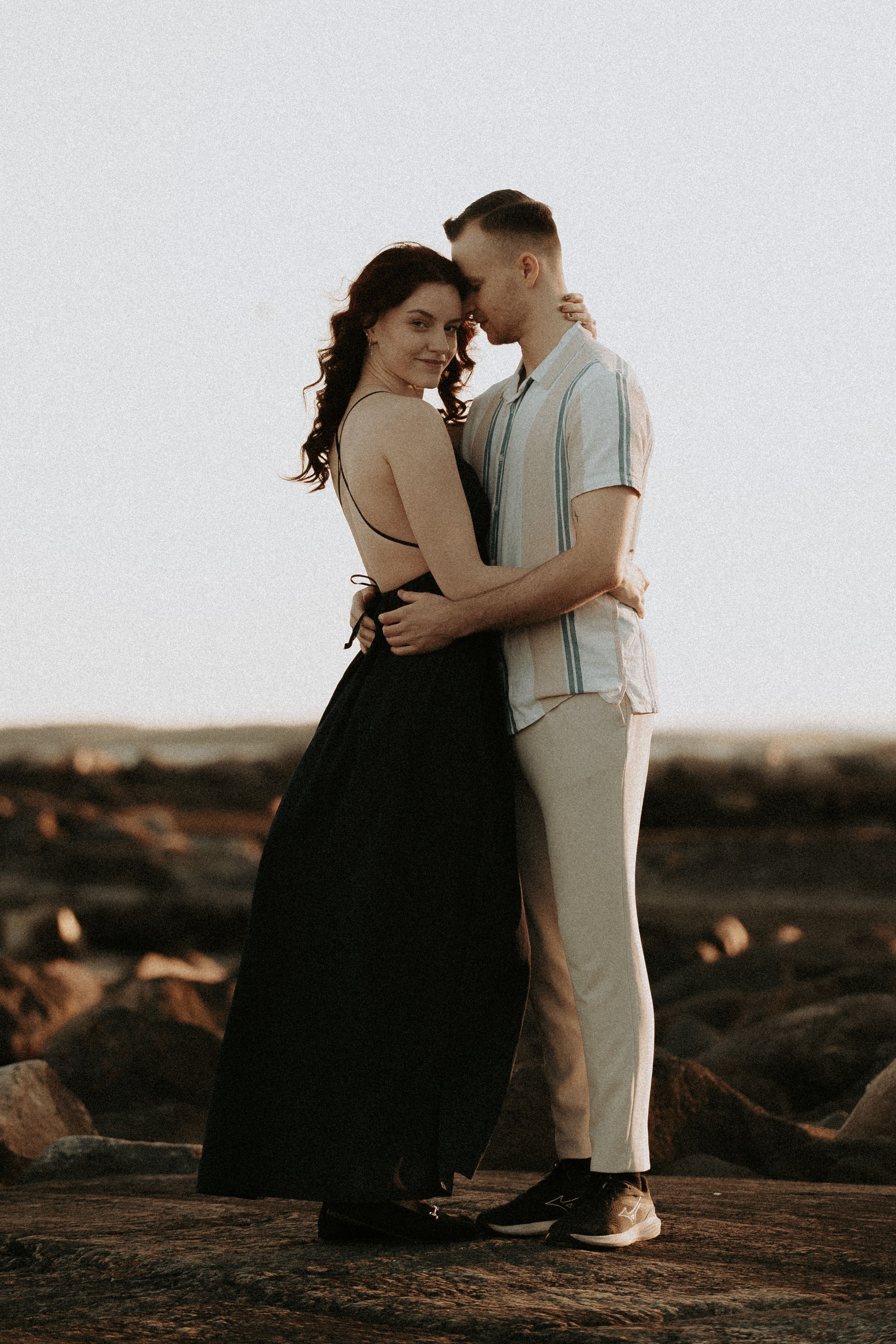 Intimate couple's portrait session on textured rocky coastline at sunset.