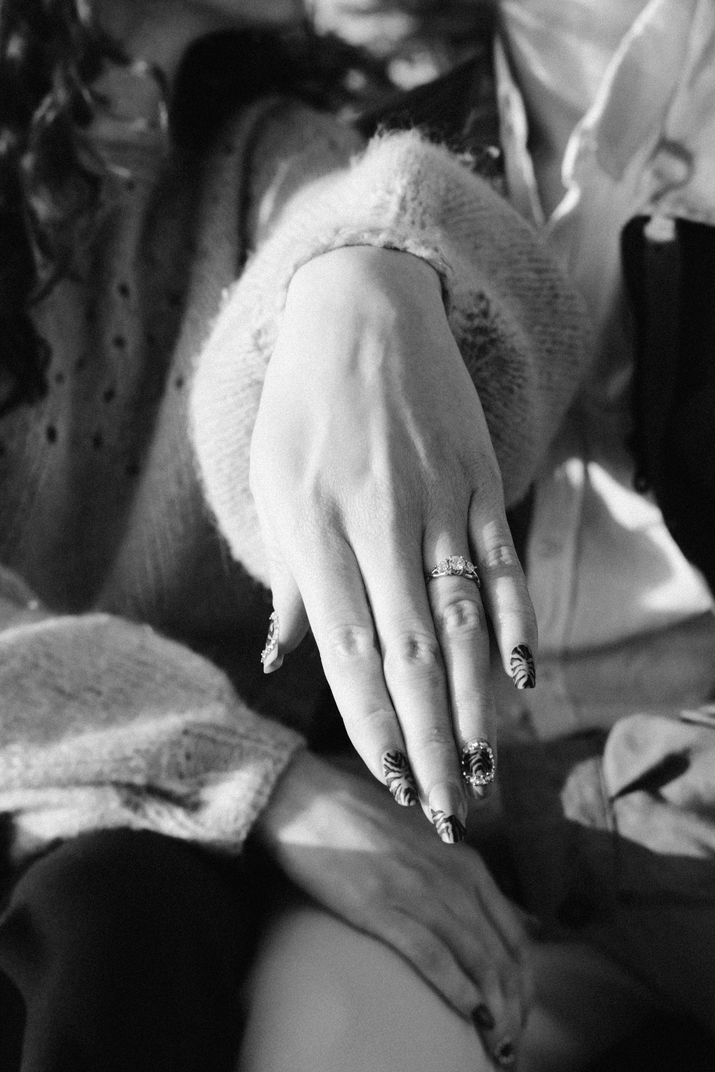 Close-up black and white photo of a hand displaying an engagement ring and decorated nails.